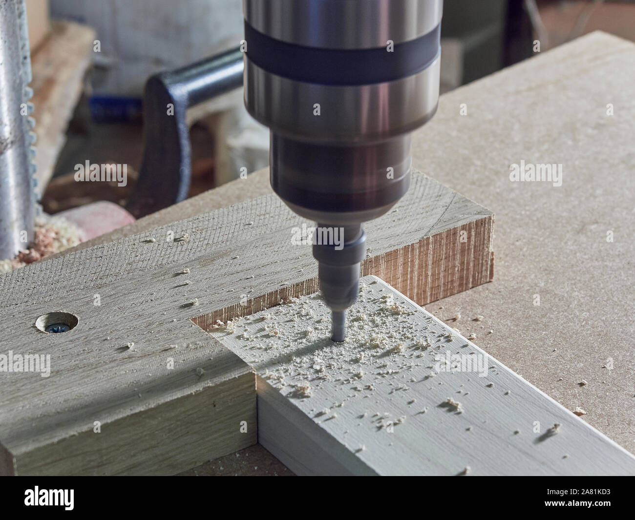 A close up of a drill bit and a chuck that belongs to a pillar drill being used to make a hole in a piece of Tulipwood in a joiners workshop, UK Stock Photo