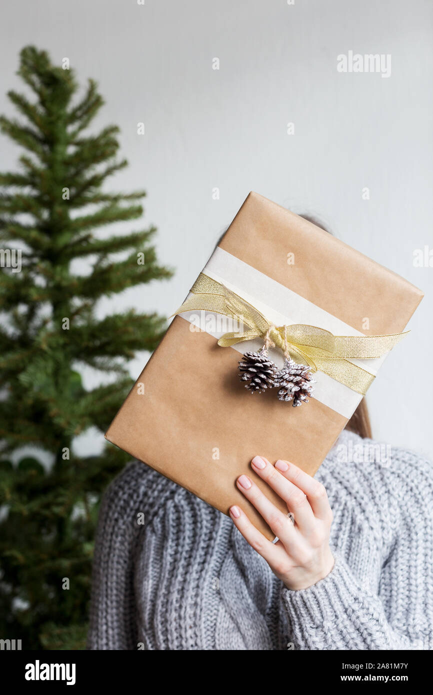 Woman hold a present box with christmas tree at background. Concept of festive surprise Stock Photo
