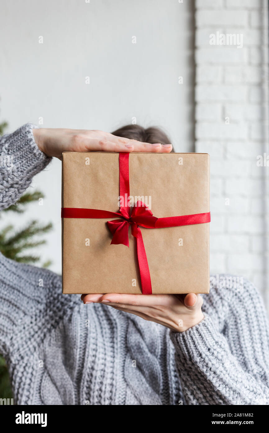 Craft paper wrapped box in hand with christmas tree at background. Concept of present surprise. Craft paper wrapped box in hand with christmas tree Stock Photo