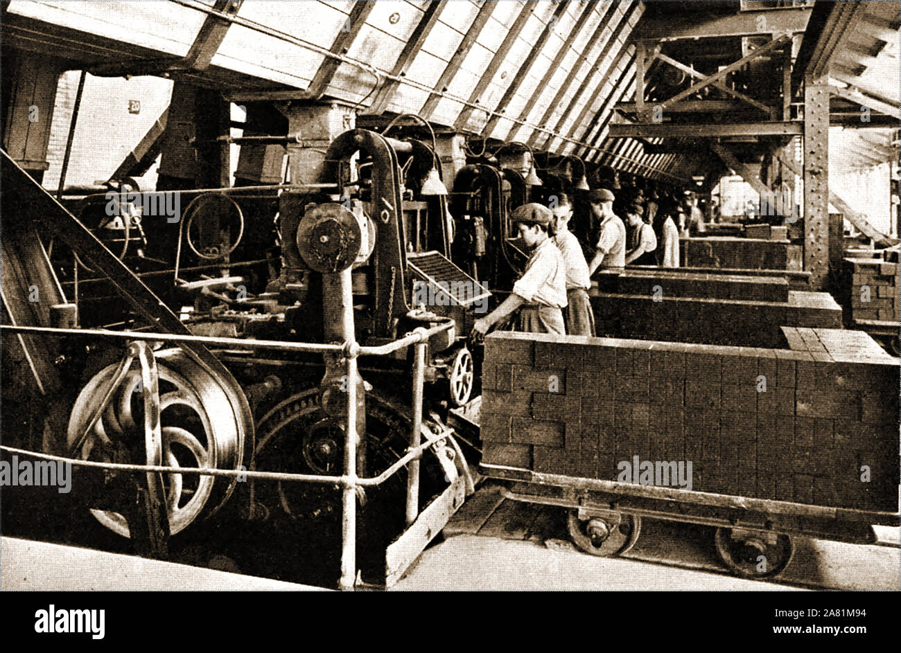 An early vintage photograph taken in the factory of the London Brick Company, UK - (early 1900s). young workers are seen loading 'green' bricks (made from lower Oxford clay ) from the moulding machine  onto trolley ready for firing in the kilns. Stock Photo