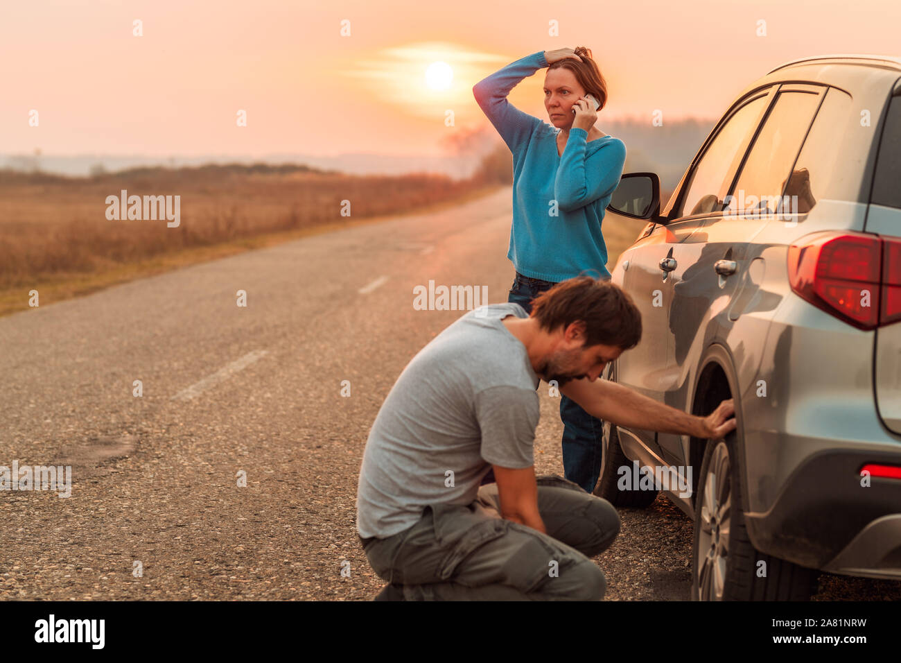 Couple repairing car flat tire on the road in autumn sunset and calling for roadside assistance, selective focus Stock Photo