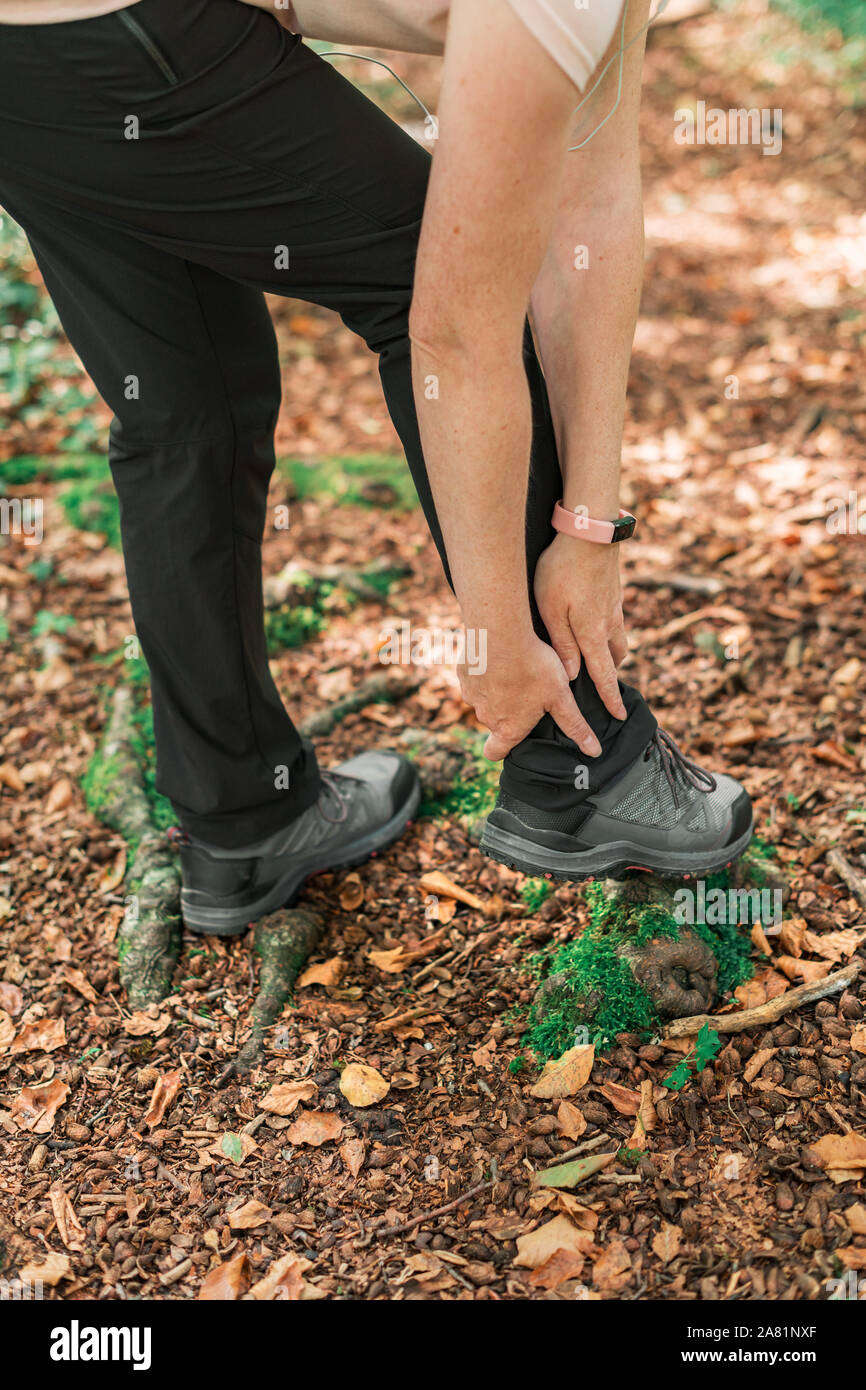 Female hiker with ankle injury in forest during outdoor trekking activity, selective focus Stock Photo