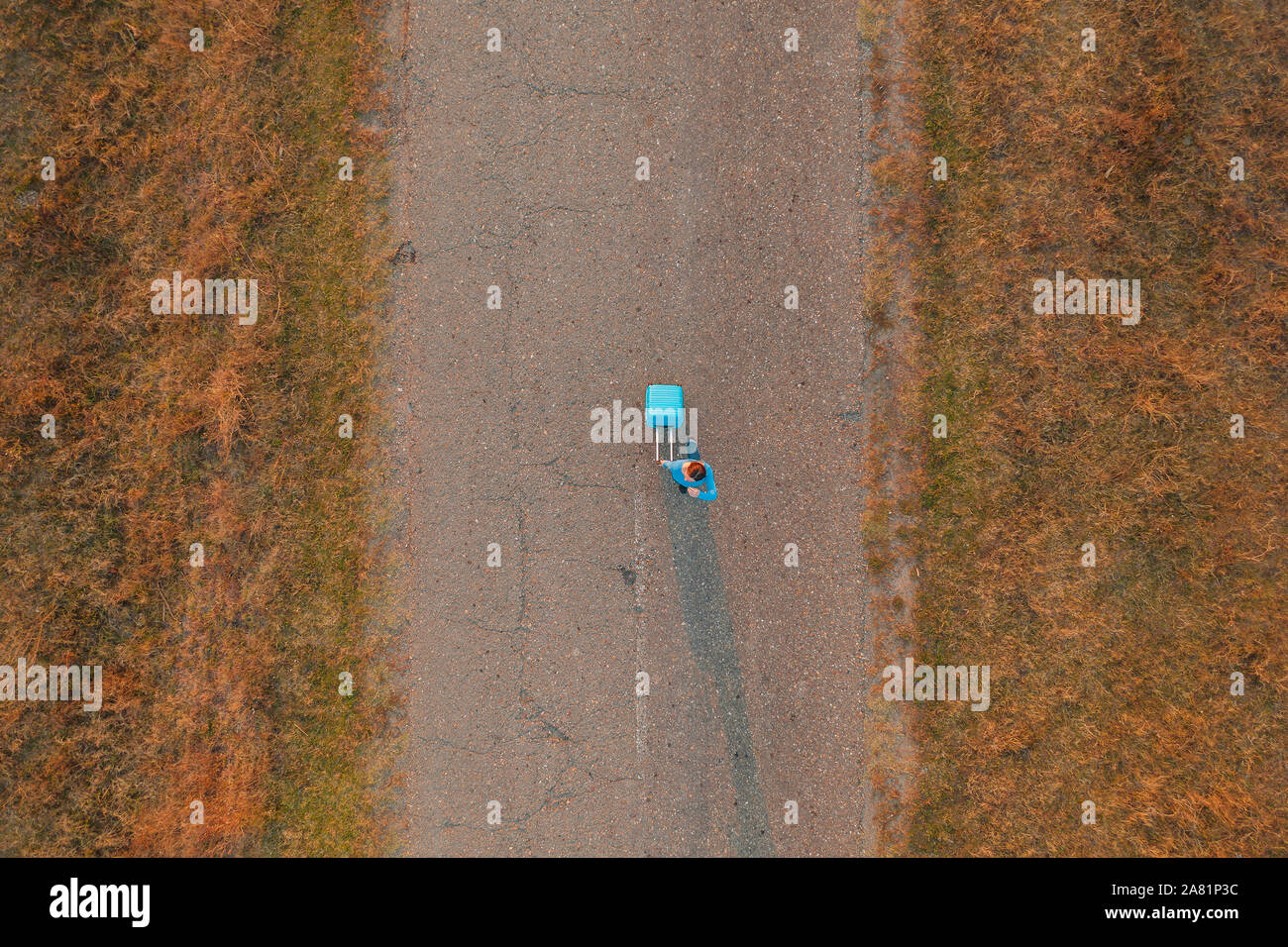Woman pulling travel suitcase luggage on road in autumn sunset, high angle view from drone pov Stock Photo