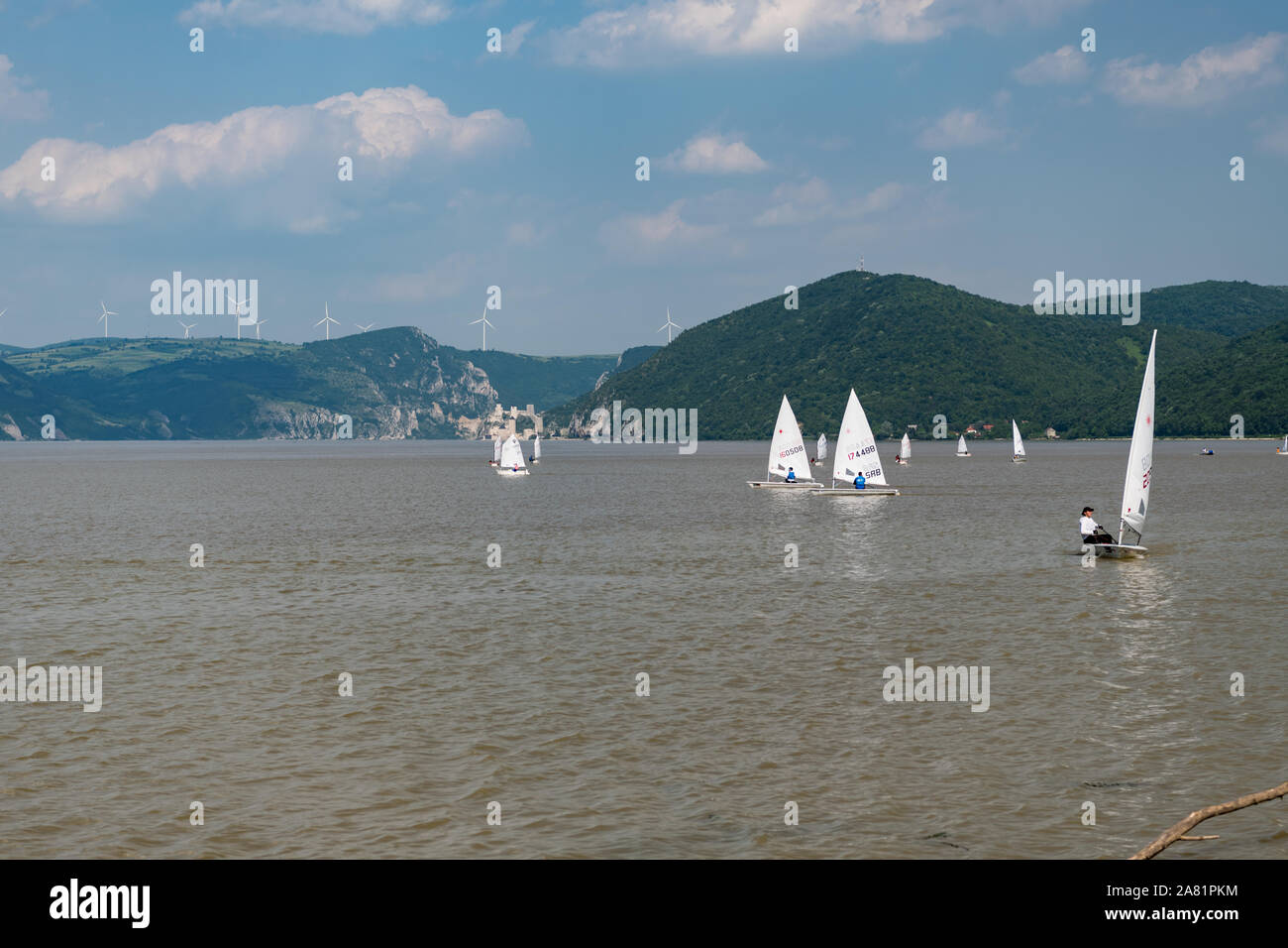 Sunny morning view of restless wather and lots of windsurfing seaboats  on the river Danube, with mountines in the background and cloudy sky high abov Stock Photo