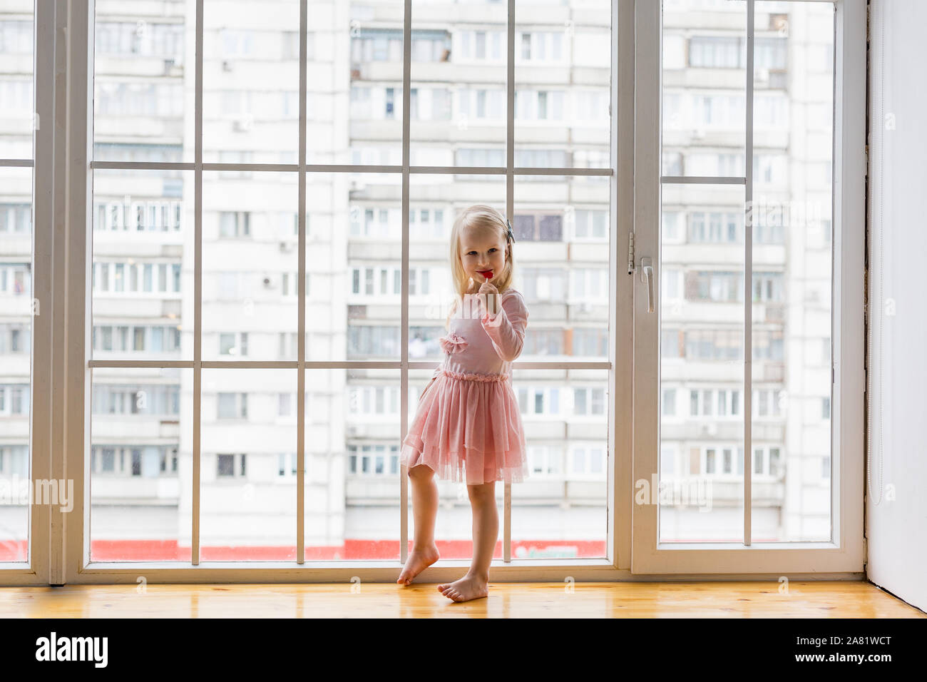 Happy little girl wearing pink dress eating lollipop while standing in ...