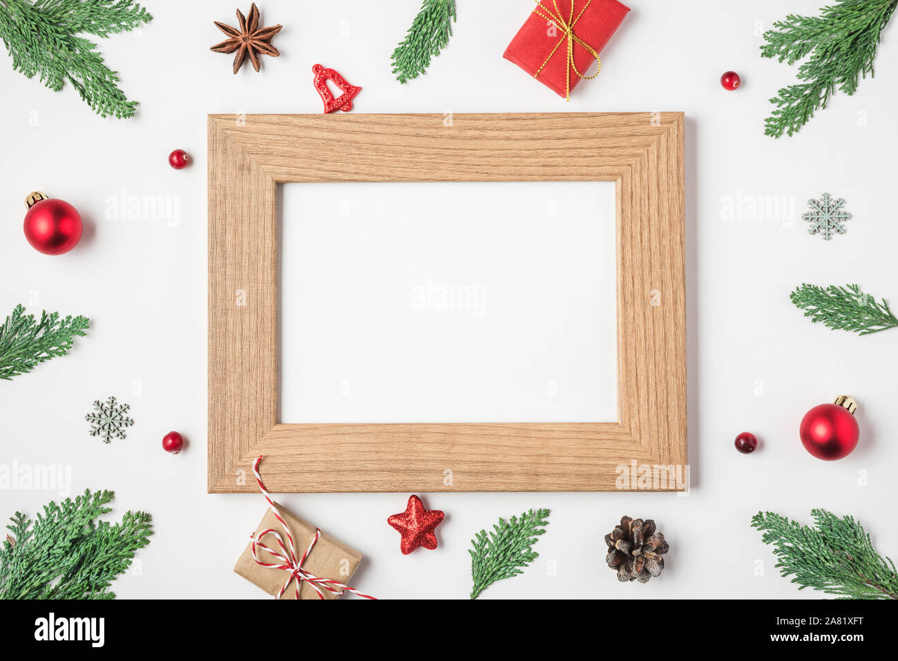 Blank Christmas photo card in frame made of fir tree branches, gift boxes, red holiday decorations on white background. mock up. flat lay. top view wi Stock Photo
