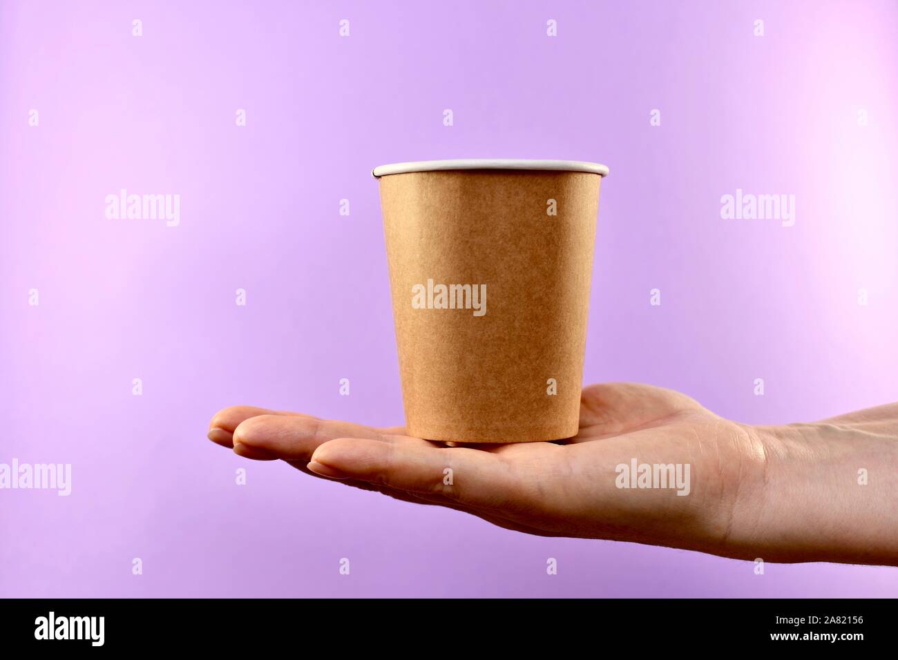 Paper cup in the palm, in the center right, on a purple background ...