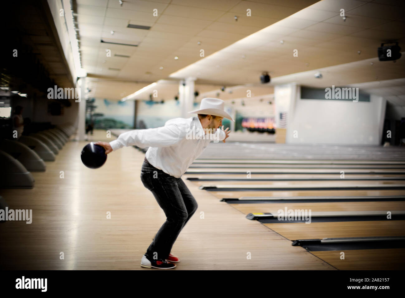 Mid-adult bearded man wearing a cowboy holding a bowling ball and preparing to through it inside a bowling alley Stock Photo - Alamy