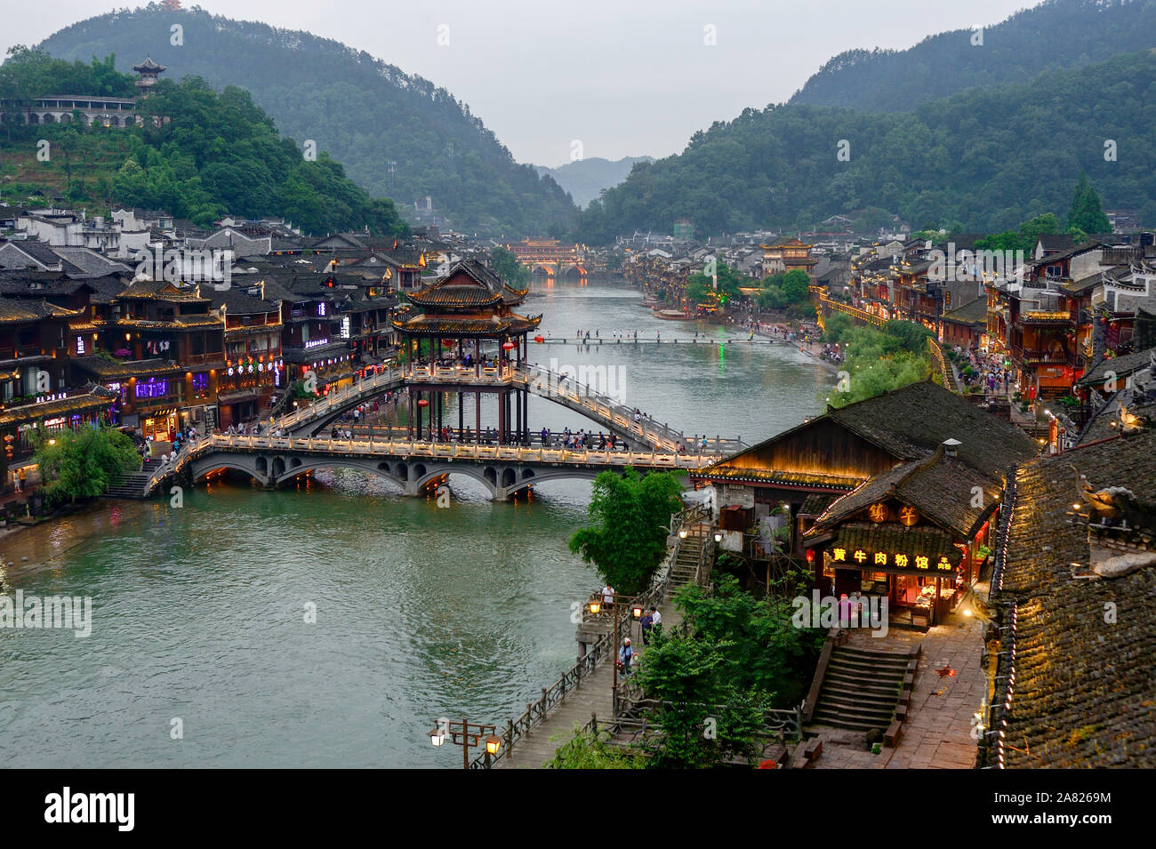 Traditional Chinese architecture flanks the tower footbridge over the Tuo Jiang River in Fenghuang Ancient City in Tibet. Stock Photo