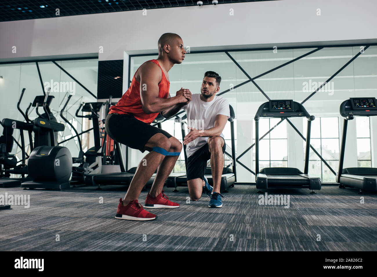 attentive trainer looking at young african american sportsman warming up in gym Stock Photo
