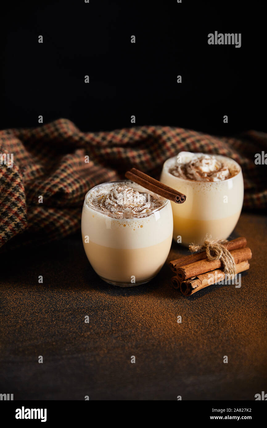 eggnog cocktail with whipped cream, cinnamon sticks and checkered cloth ...