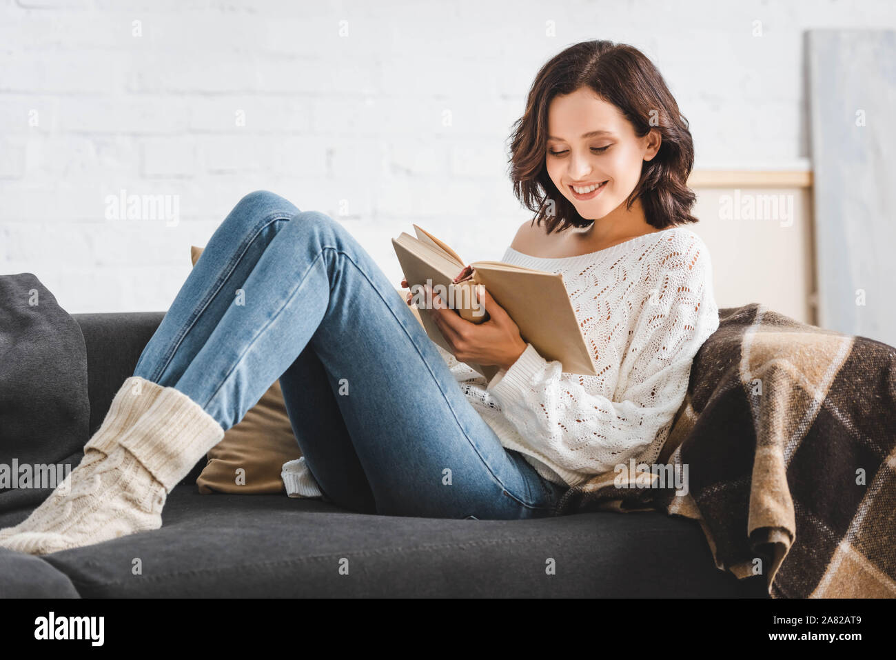 smiling girl reading book on sofa at home Stock Photo - Alamy