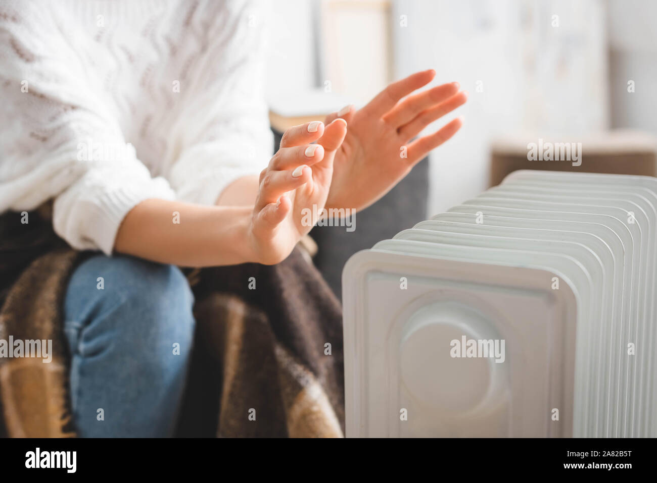 Partial View Of Girl Warming Up With Heater In Cold Room