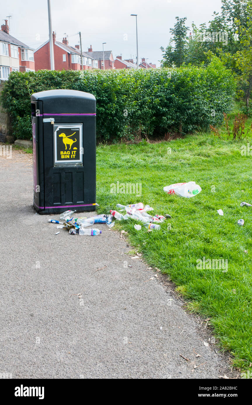 Litter bin with Enviromental litter or rubbish thrown on the ground next to it. Glass bottles tin cans plastic bags plastic bottles and paper Stock Photo