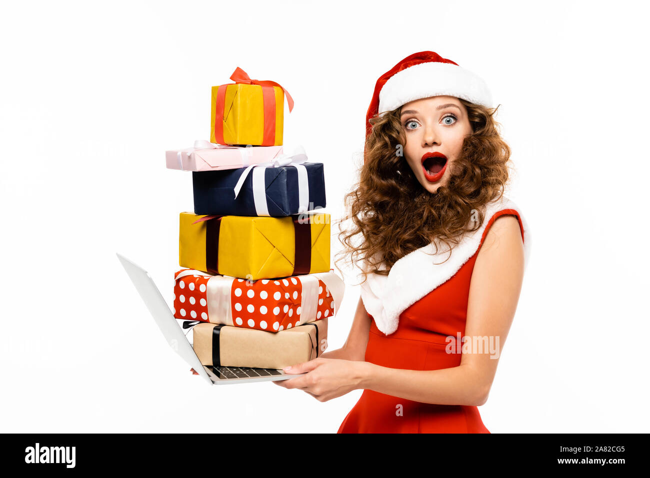 shocked girl in santa costume holding laptop with pile of gifts, isolated on white Stock Photo