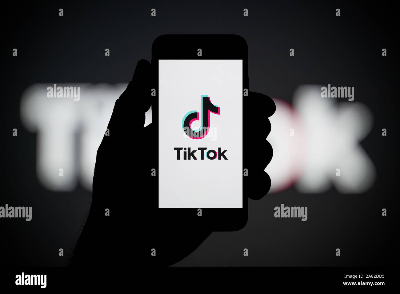A man looks at his iPhone which displays the TikTok logo, with the same logo in the background (Editorial use only). Stock Photo