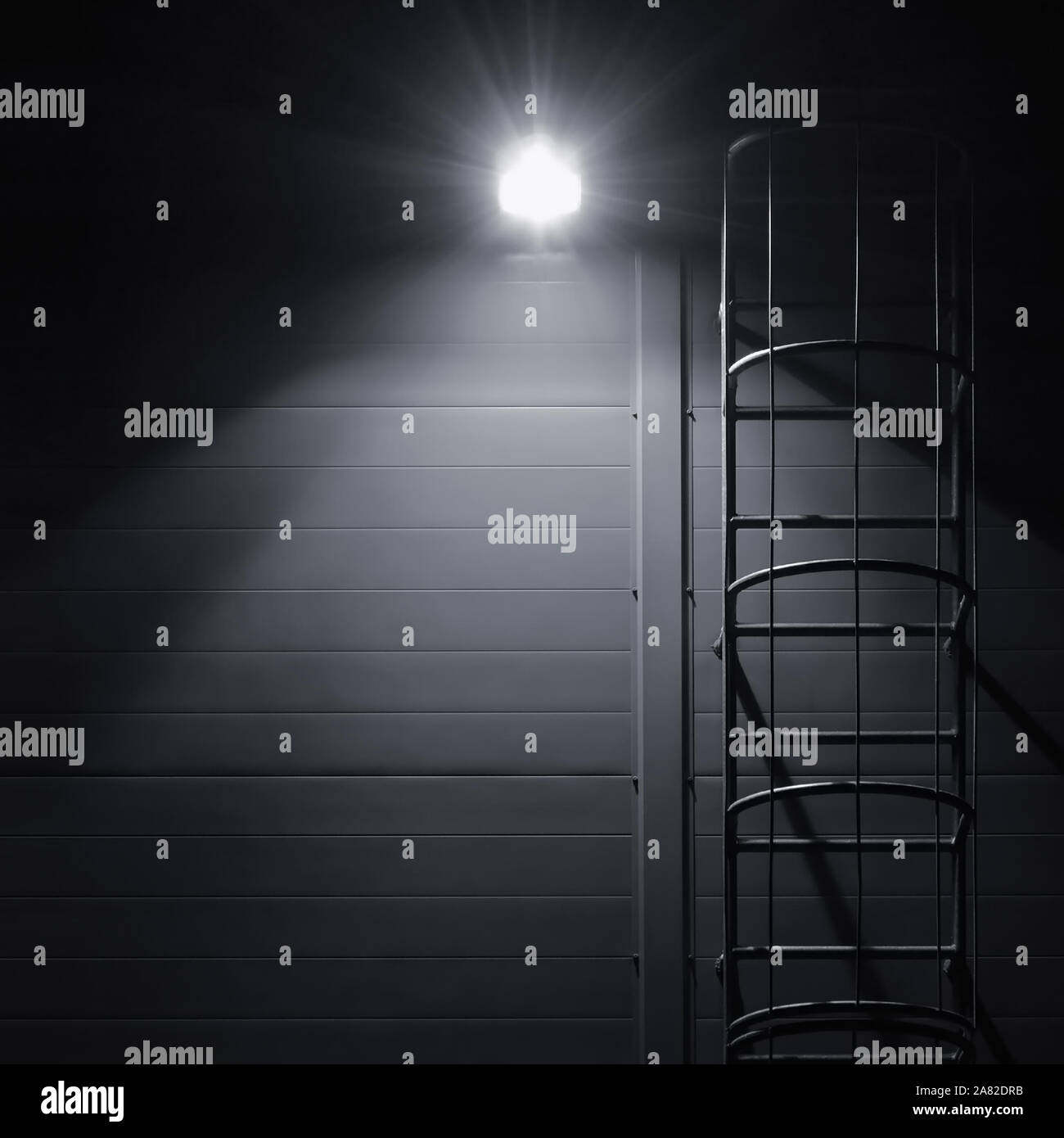 Fire emergency rescue access escape ladder stairway, roof maintenance stairs at night, bright shining lantern lamp light illumination glow shadows Stock Photo