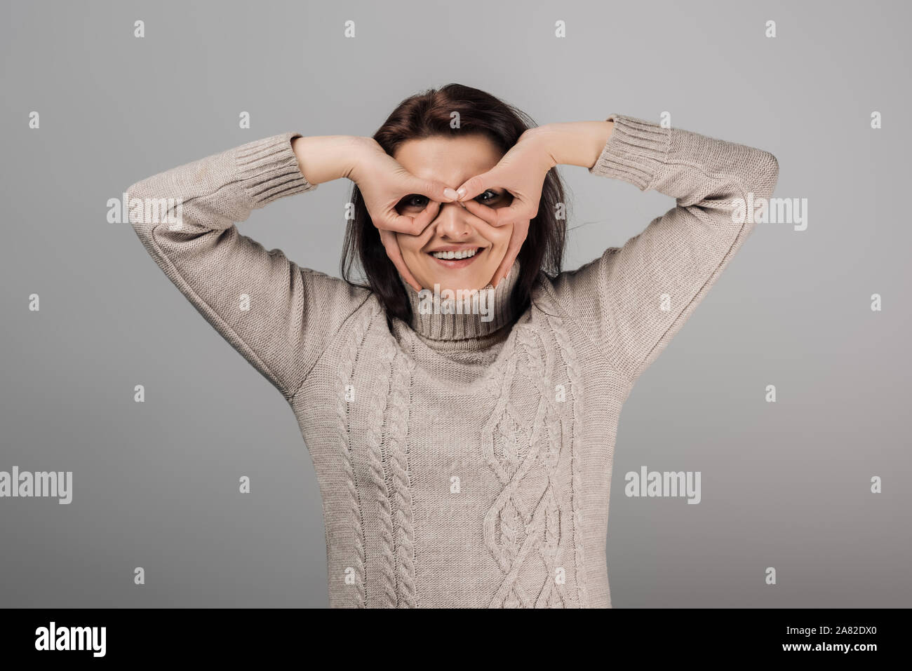 cheerful woman cowering face and smiling isolated on grey Stock Photo