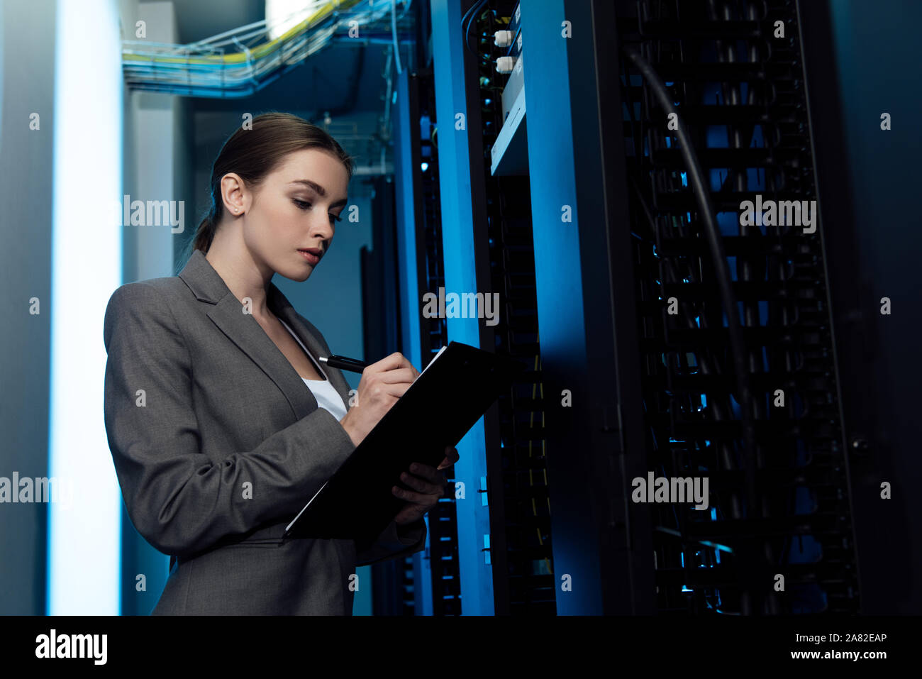 attractive businesswoman writing while holding clipboard in server room