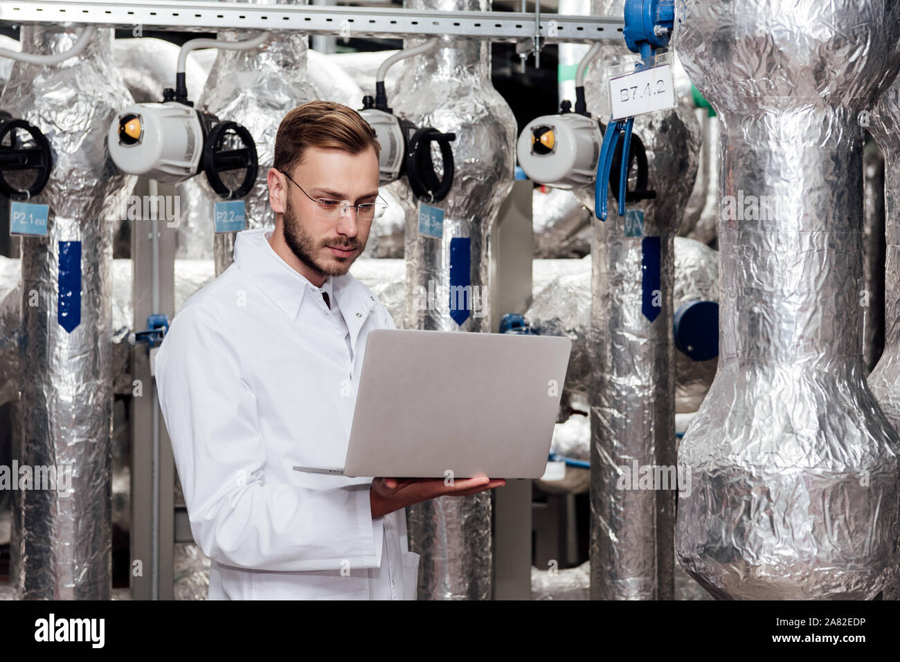 handsome bearded engineer in white coat holding laptop Stock Photo