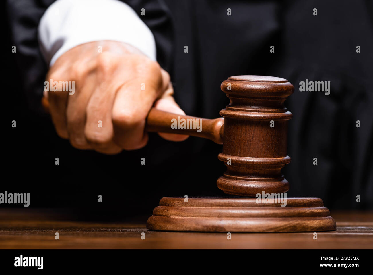 cropped view of judge in judicial robe sitting at table and hitting with gavel Stock Photo