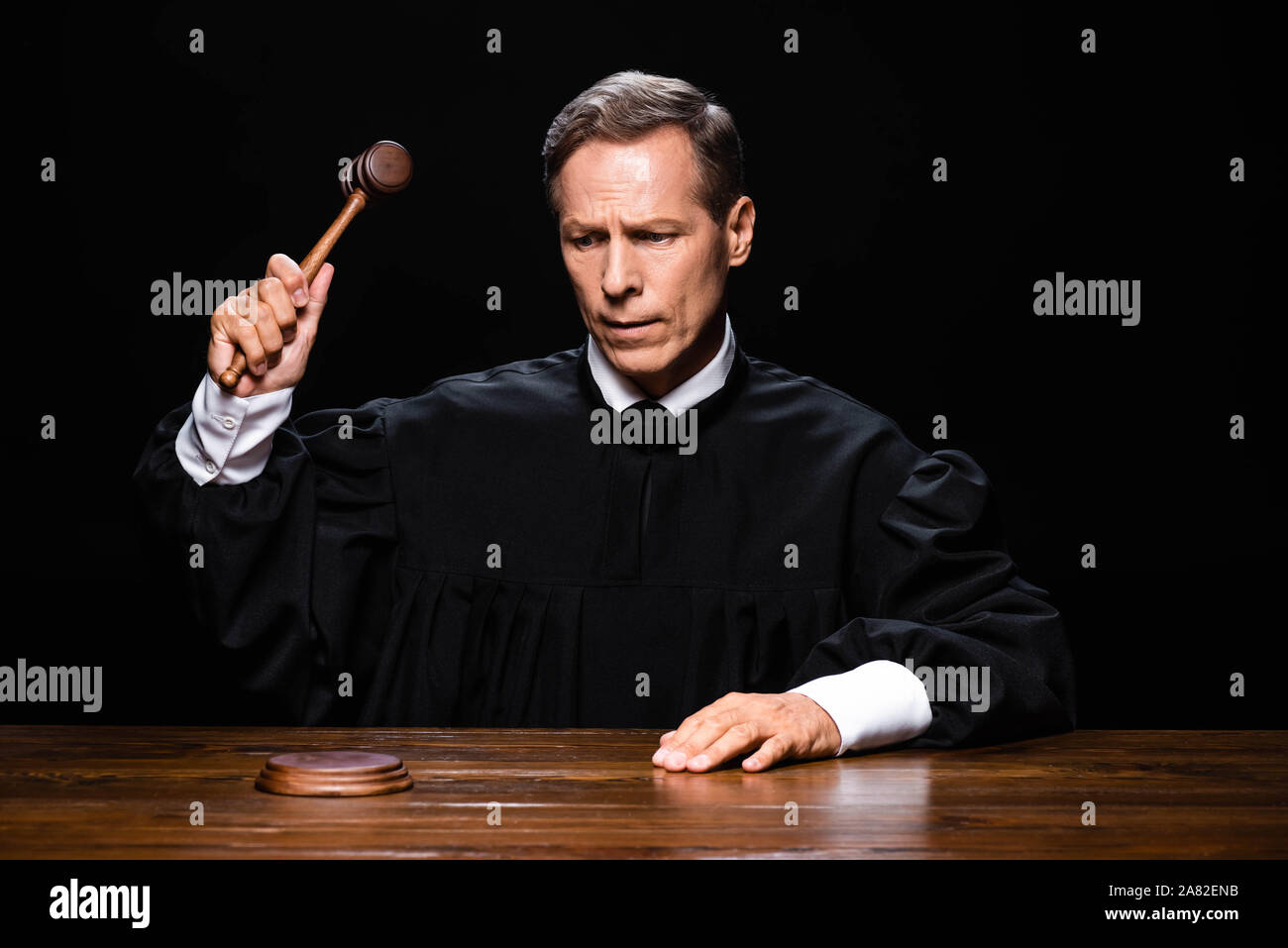 judge in judicial robe sitting at table and hitting with gavel isolated