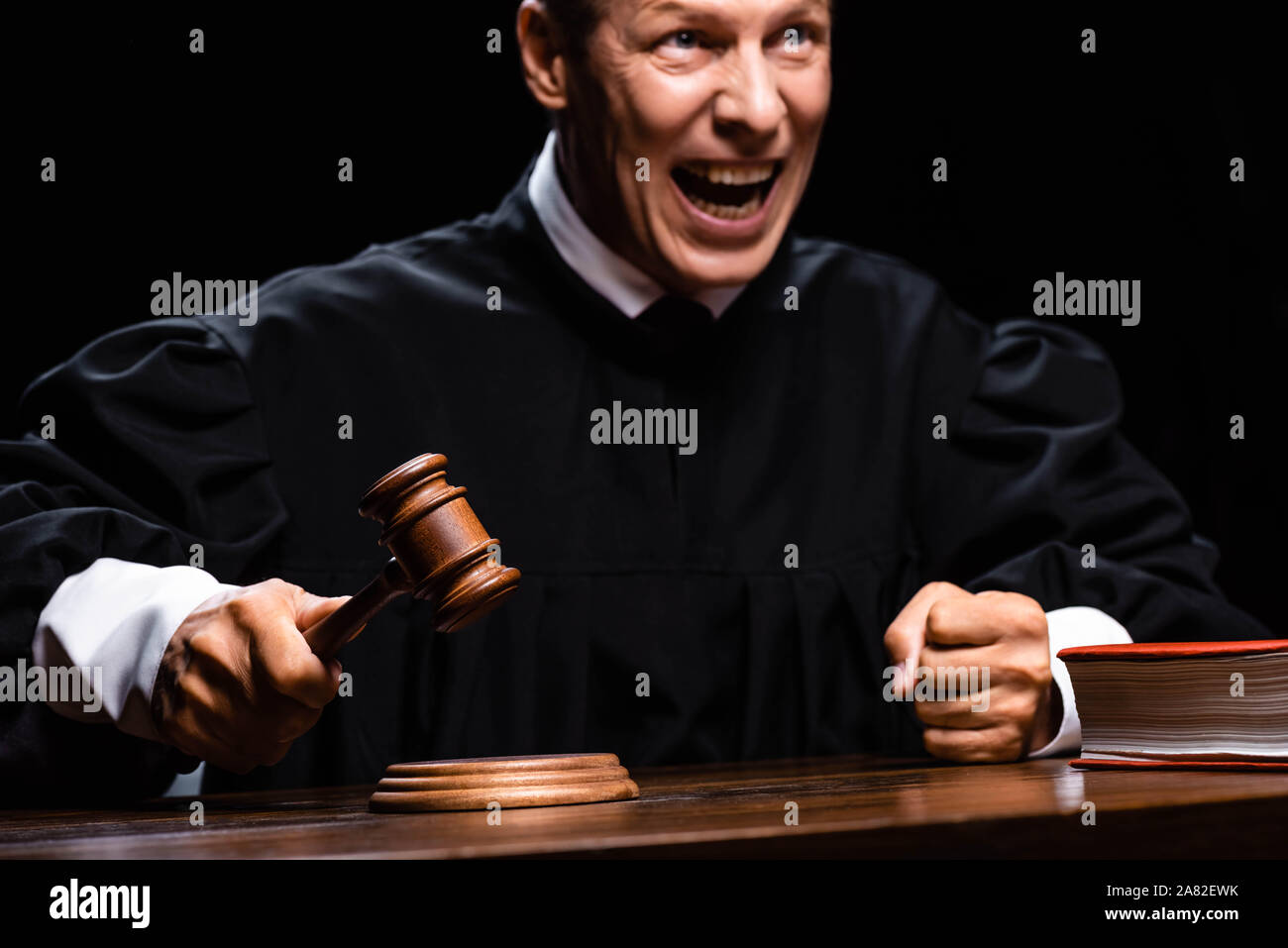angry judge in judicial robe sitting at table and hitting with gavel