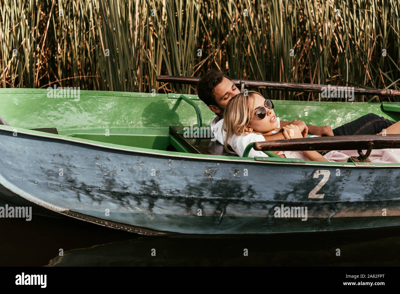 young couple relaxing in boat on river near thicket of sedge Stock Photo