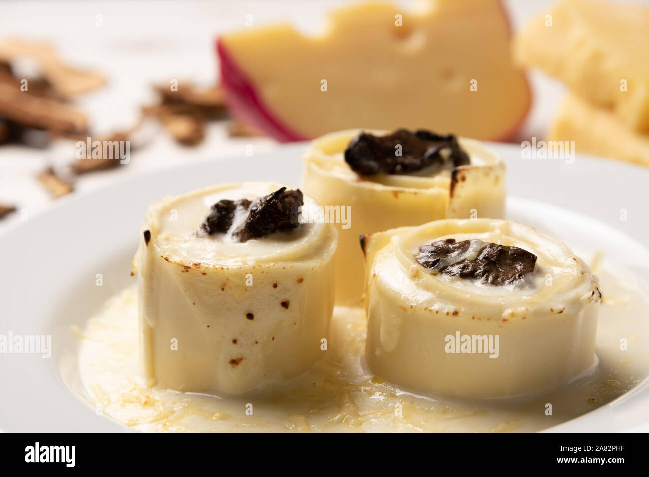 Homemade rondelli with four cheese and mushuroom sauce in white plate on rustic white wooden table background, soft light Stock Photo