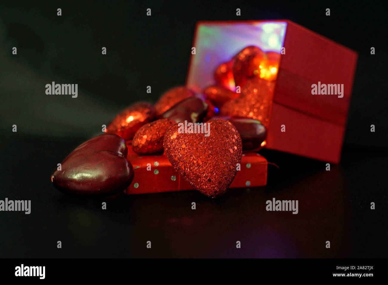 Valentines day heart shapes spilling from the colorfully lit interior of a red gift box  on a black background with selective focus Stock Photo