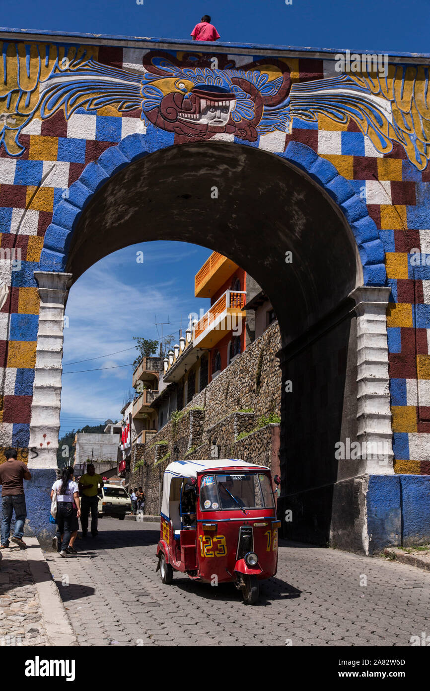 A mototaxi, an economical form of public transportation in Guatemala, passing through the colorful archway gate in Chichicastenango, Guatemala. Stock Photo