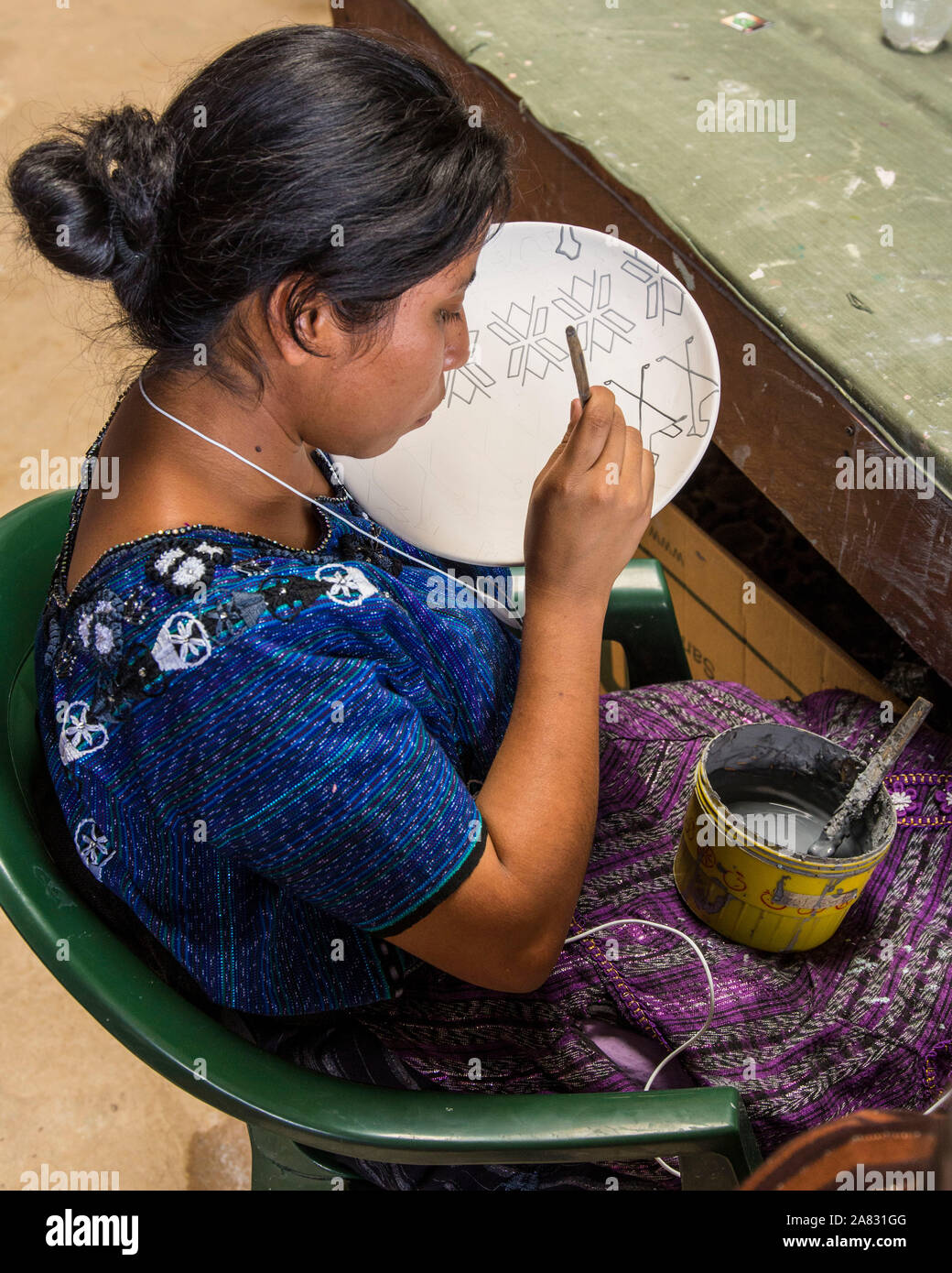 A young Mayan woman, wearing typical traditional dress, paints designs