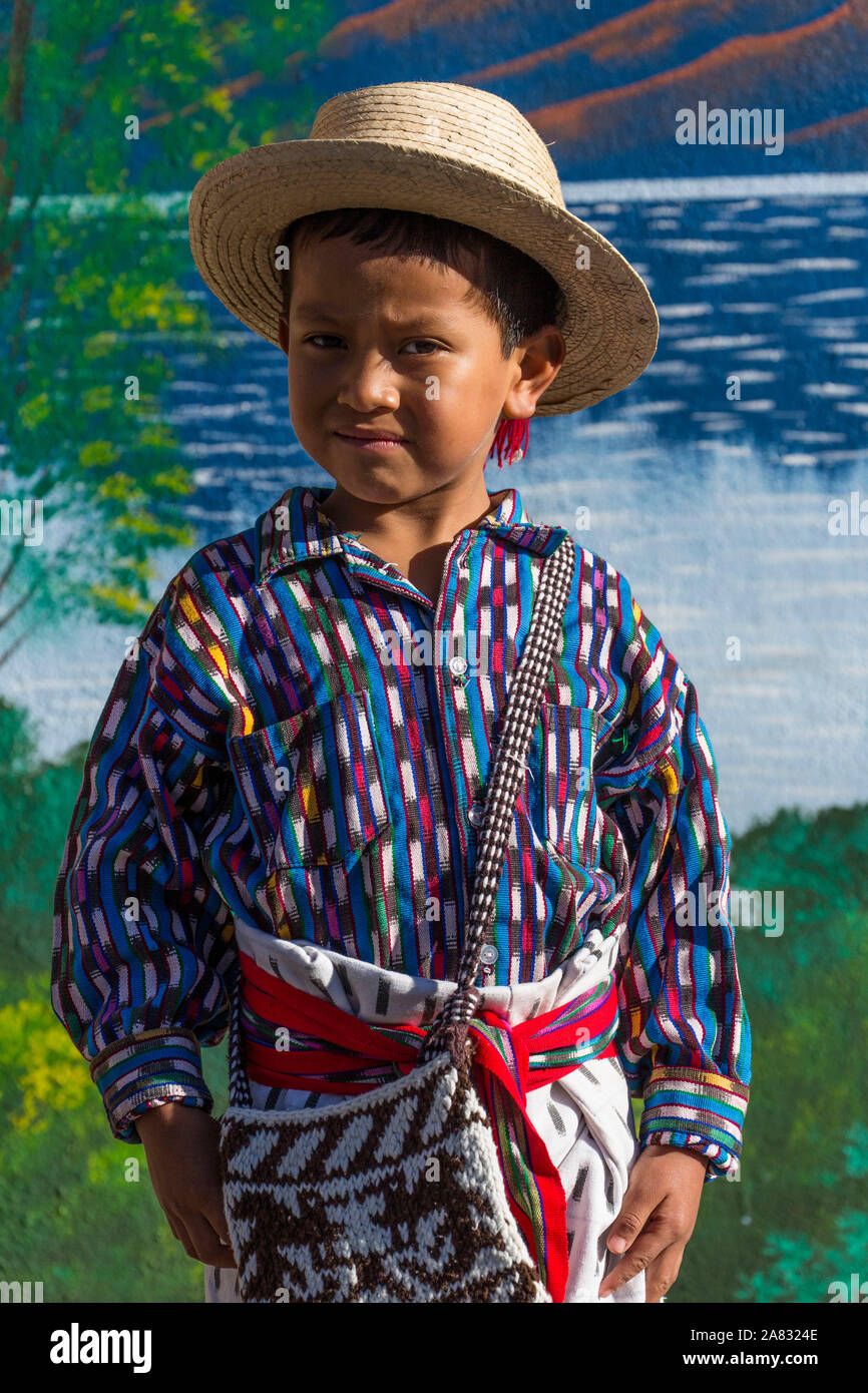 Young Mayan boy, age 6, wearing traditional dress of San Pedro la Laguna, Guatemala, poses for a portrait in front of a painted wall with a scene of L Stock Photo