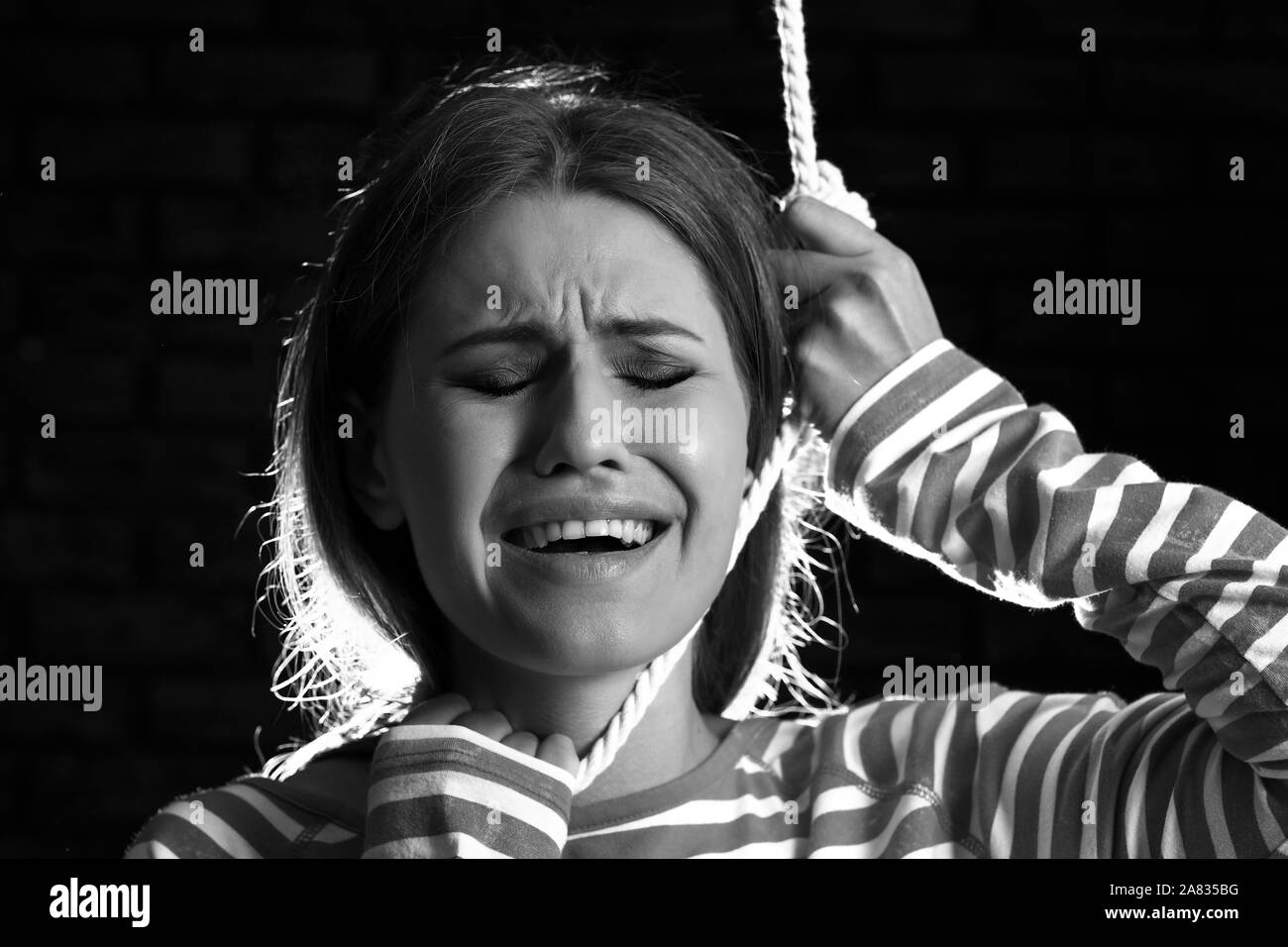 Black and white photo of woman with noose around neck on dark background. Suicide concept Stock Photo