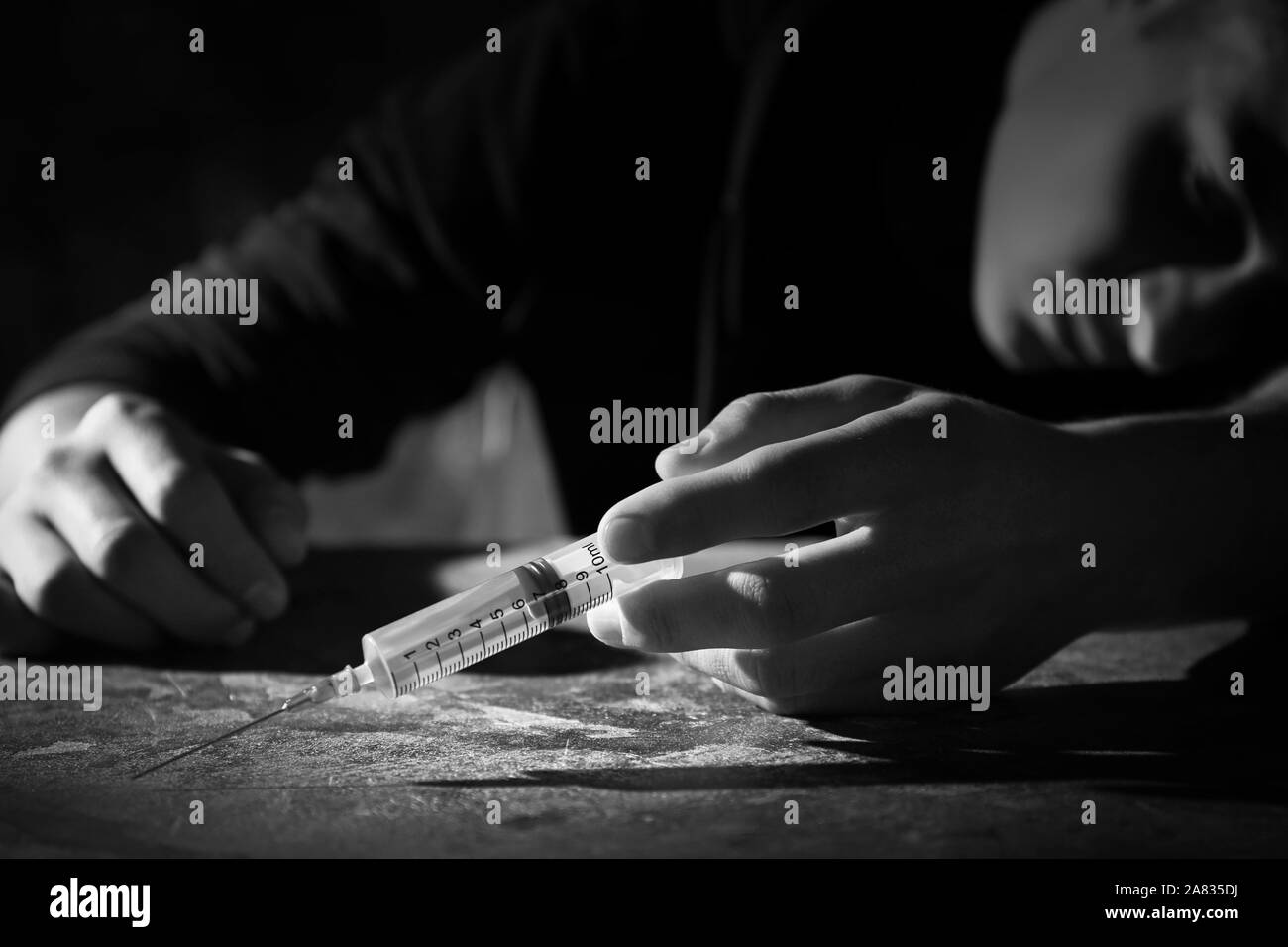 Black and white photo of male suicider with syringe at table Stock Photo