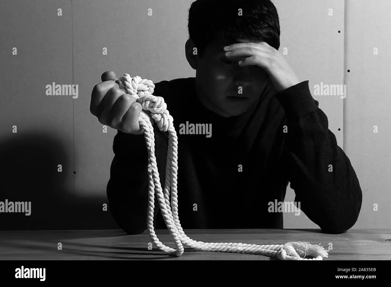 Black and white photo of depressed man with rope thinking about suicide at home Stock Photo