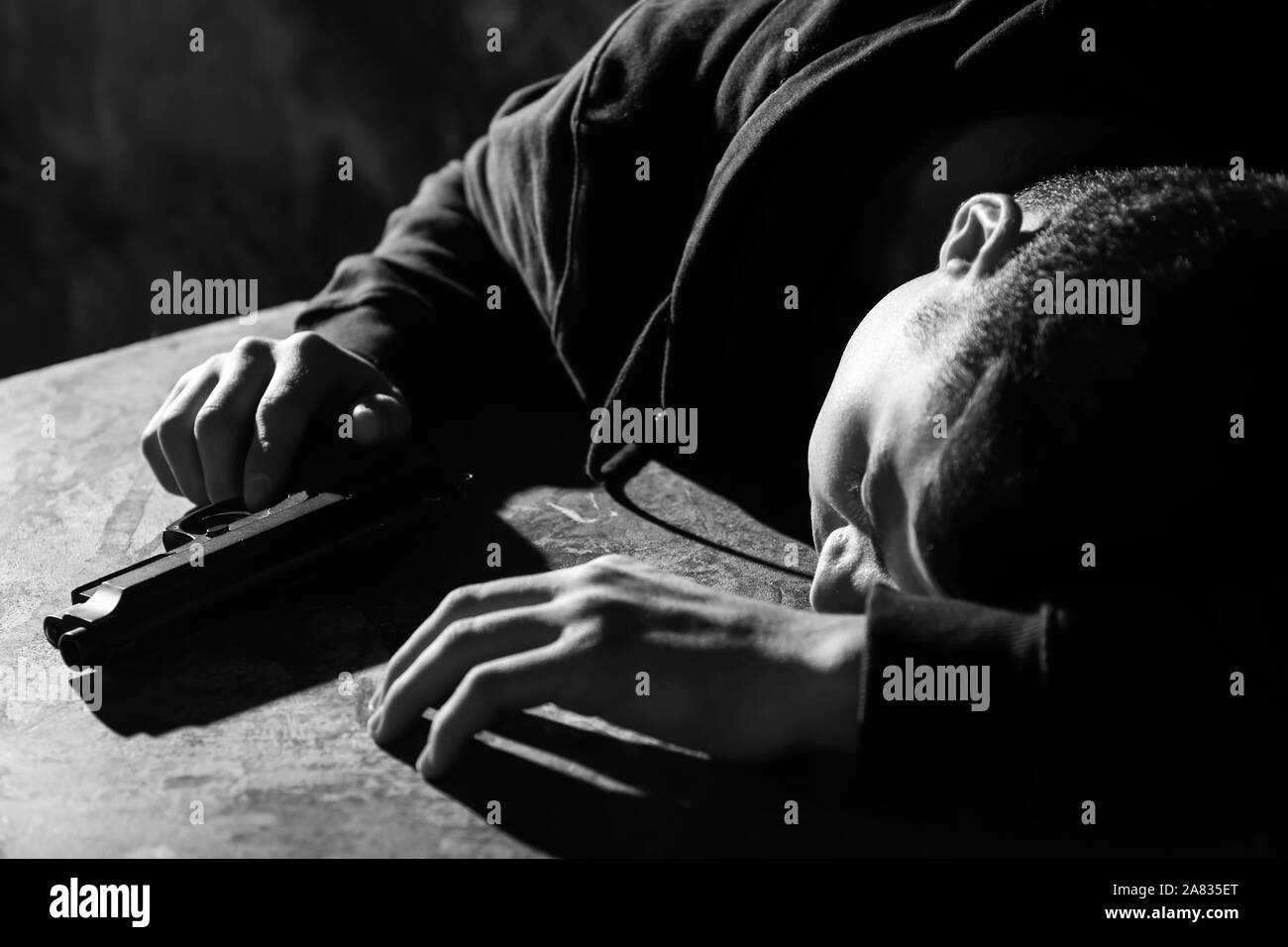 Black and white photo of depressed young man with gun at table. Suicide concept Stock Photo