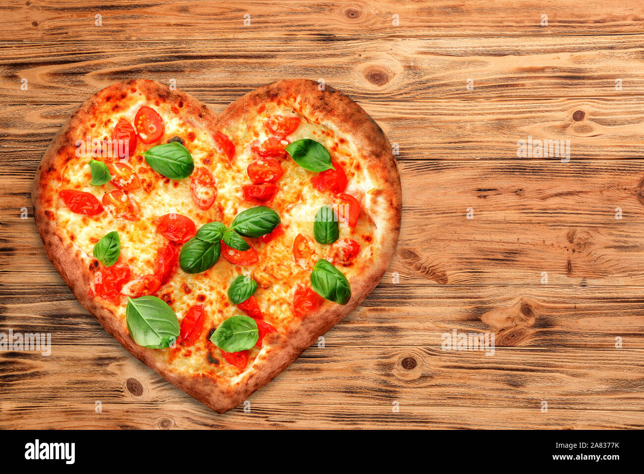 Tasty heart-shaped pizza on wooden background Stock Photo