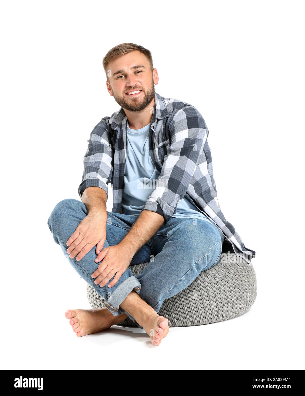 Handsome young man sitting on pouf against white background Stock Photo ...