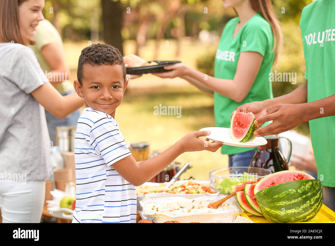 Little African-American poor boy receiving food from volunteer outdoors Stock Photo