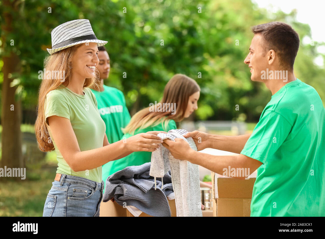 Young volunteer giving new clothes for poor woman outdoors Stock Photo