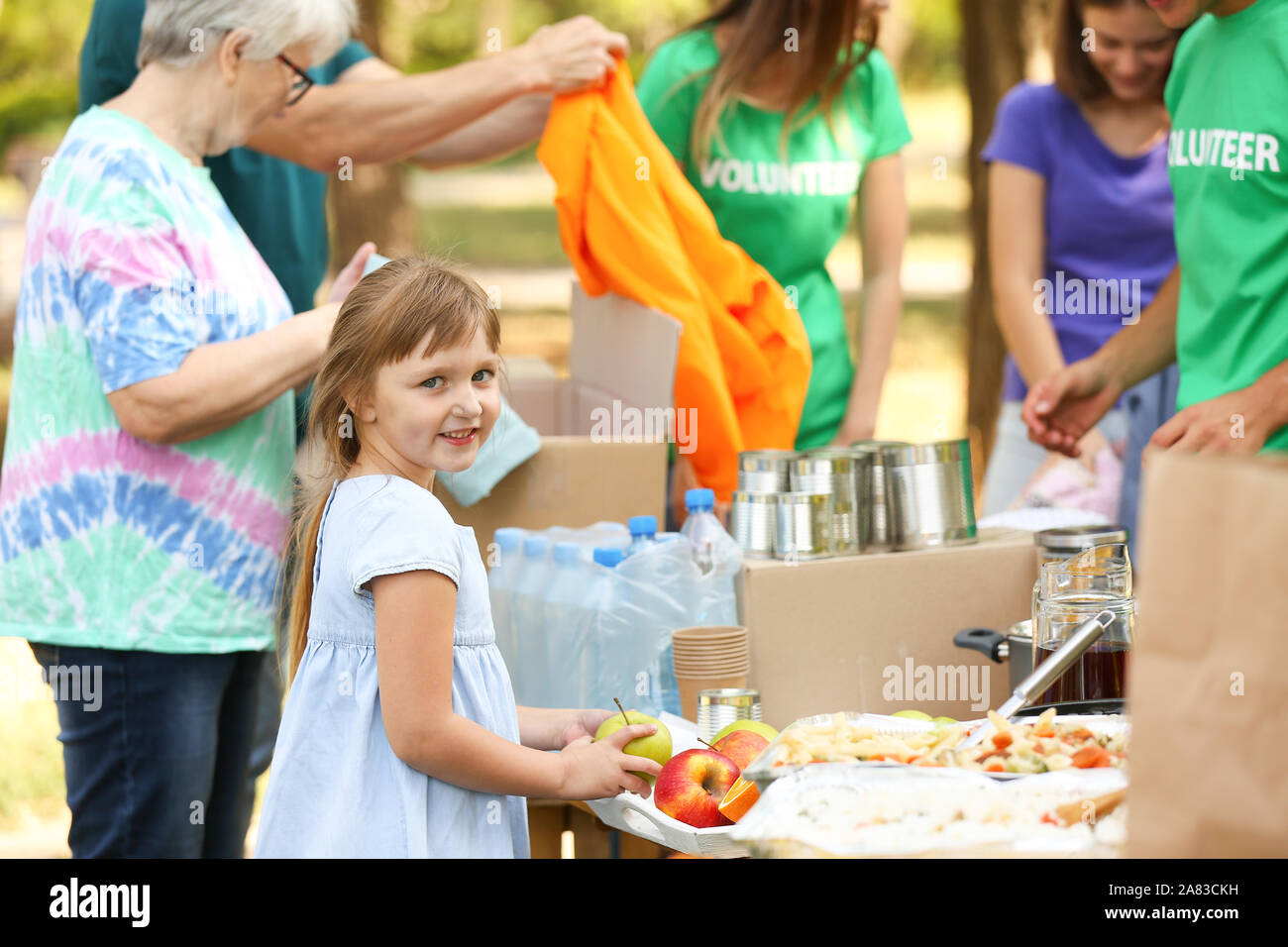 Little poor girl receiving food from volunteers outdoors Stock Photo