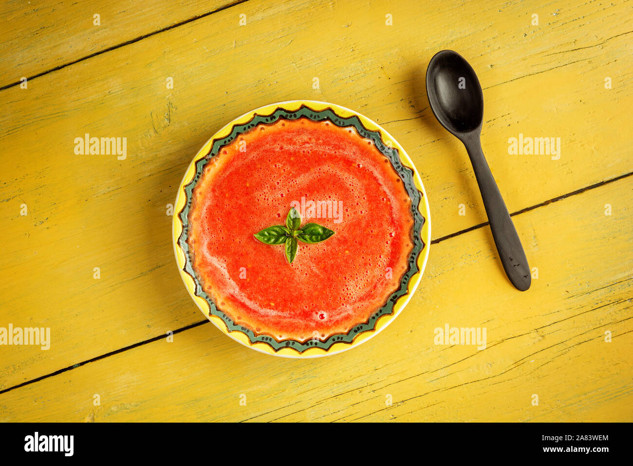Gazpacho soup with green basil in yellow bowl on rustic background