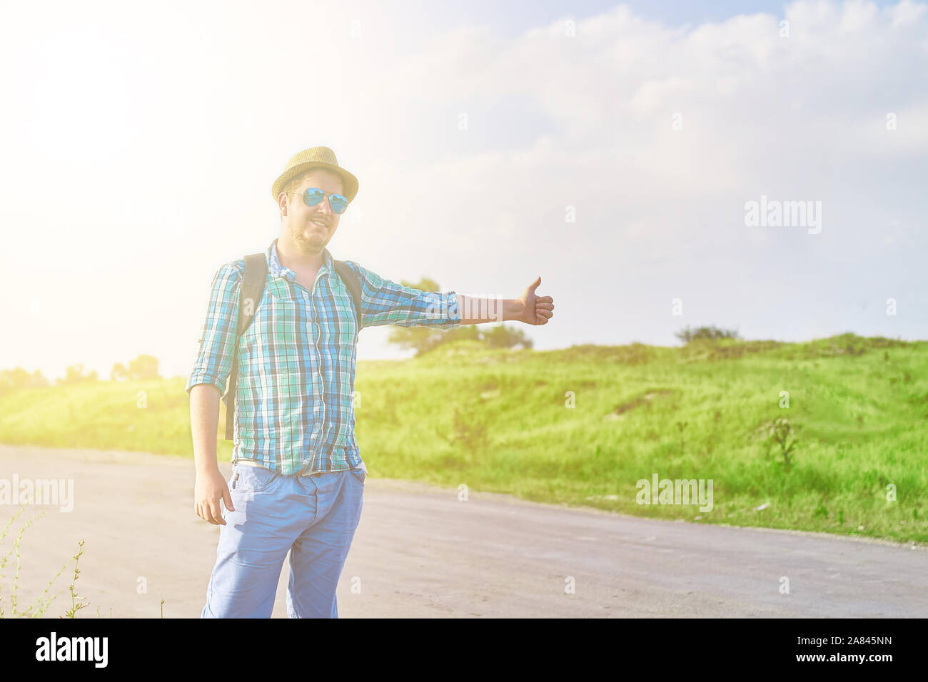 Hitchhiker with backpack in summer hat, light shirt, shorts on the road in  tropical country in Sunny weather at summer Stock Photo - Alamy