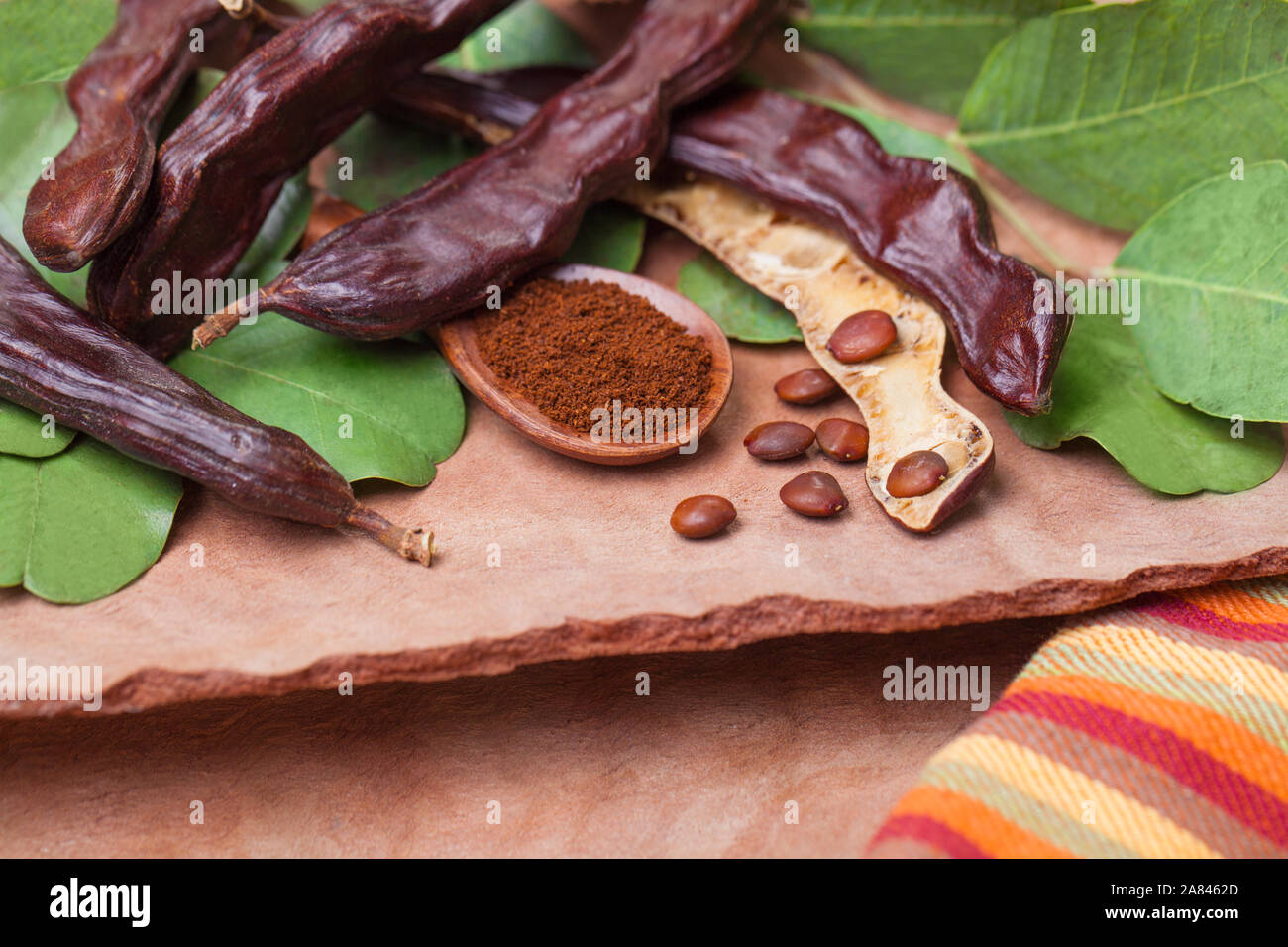 Carob. Organic carob pods with seeds and leaves on tree bark table