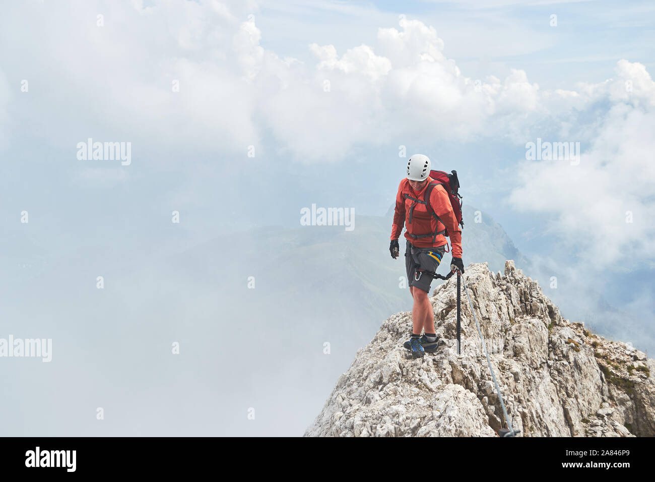 Man on a narrow mountain ridge surrounded by fog, up on via ferrata Eterna (Cadore Brigade) at Marmolada, Dolomites mountain range, Italy.  Copy space Stock Photo