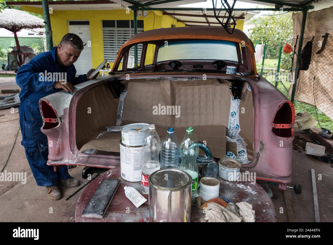 A Cuban car body repairer, working on a classic car in a small village garage in the Valle de Vinales, Pinar del R’o Province, west Cuba, Cuba Stock Photo