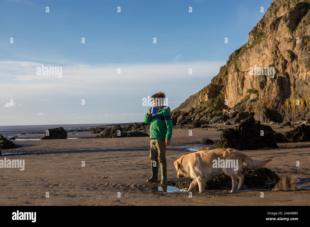 A young boy drinking hot chocolate on an empty beach, UK Stock Photo