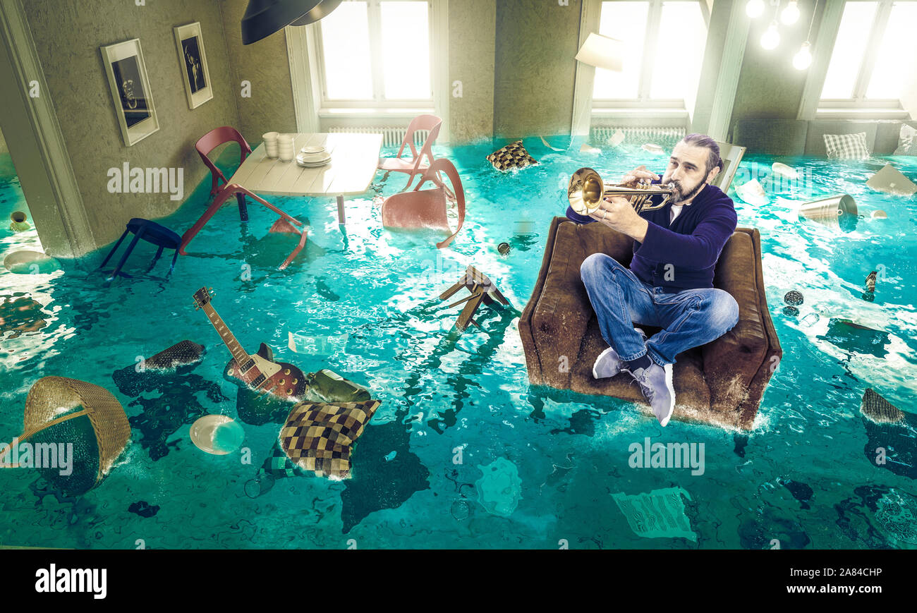 man plays the trumpet in a floating chair in a completely flooded living room. regardless of the situation, he only thinks of music. Stock Photo