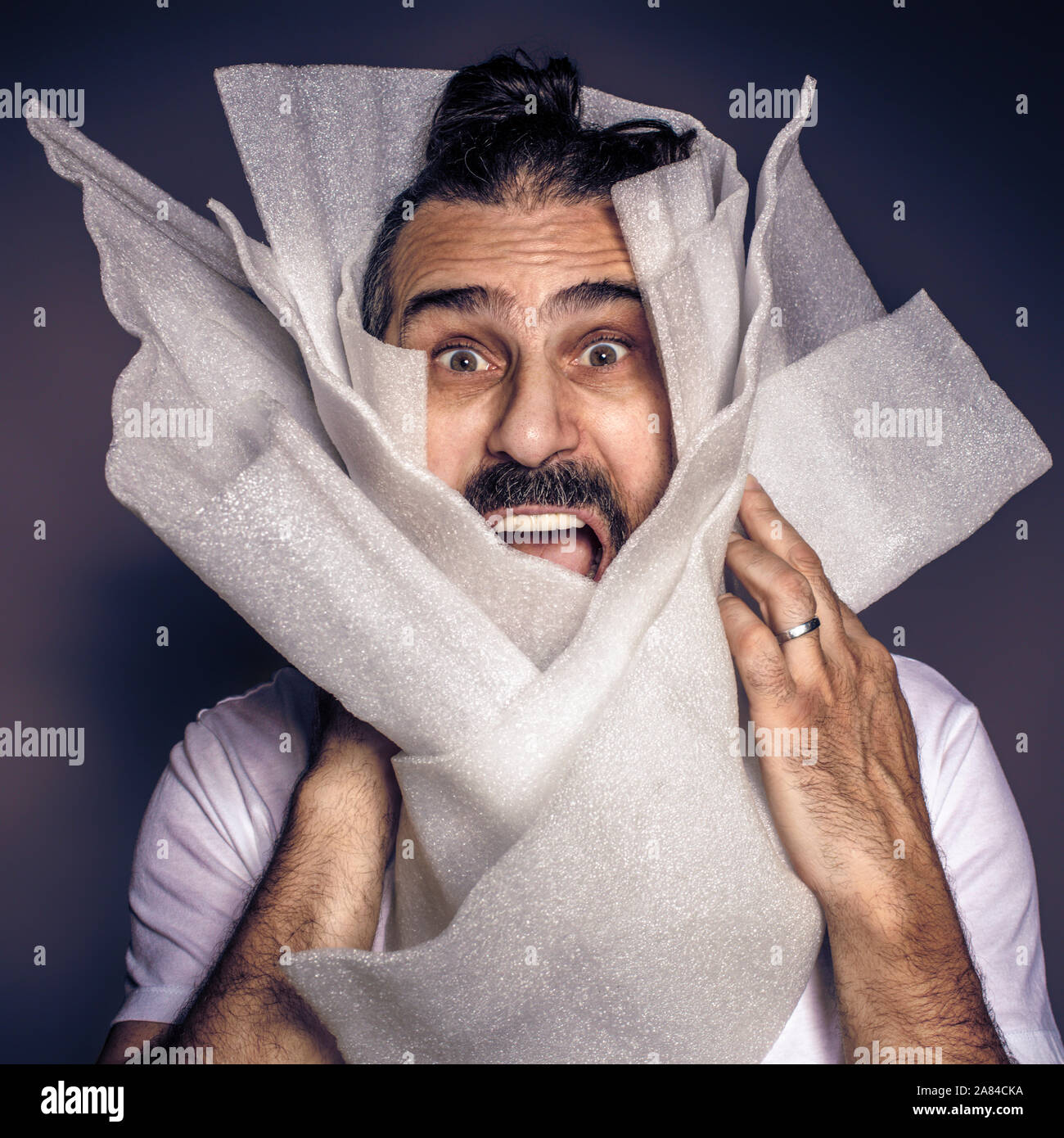 man with long hair and beard screams wrapped in plastic packaging. Sensitization on plastic overuse. Stock Photo